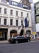 A black car parked in front of a building with a flagDescription automatically generated with low confidence